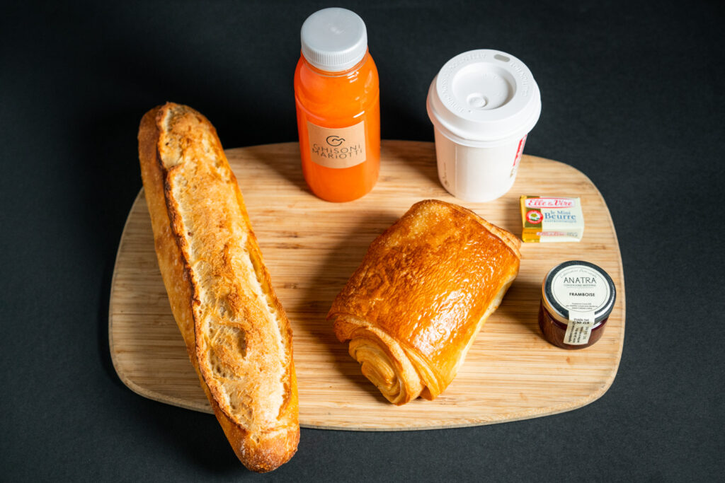 Photo du petit déjeuner, avec une baguette, une viennoiserie, une boisson chaude et un jus.